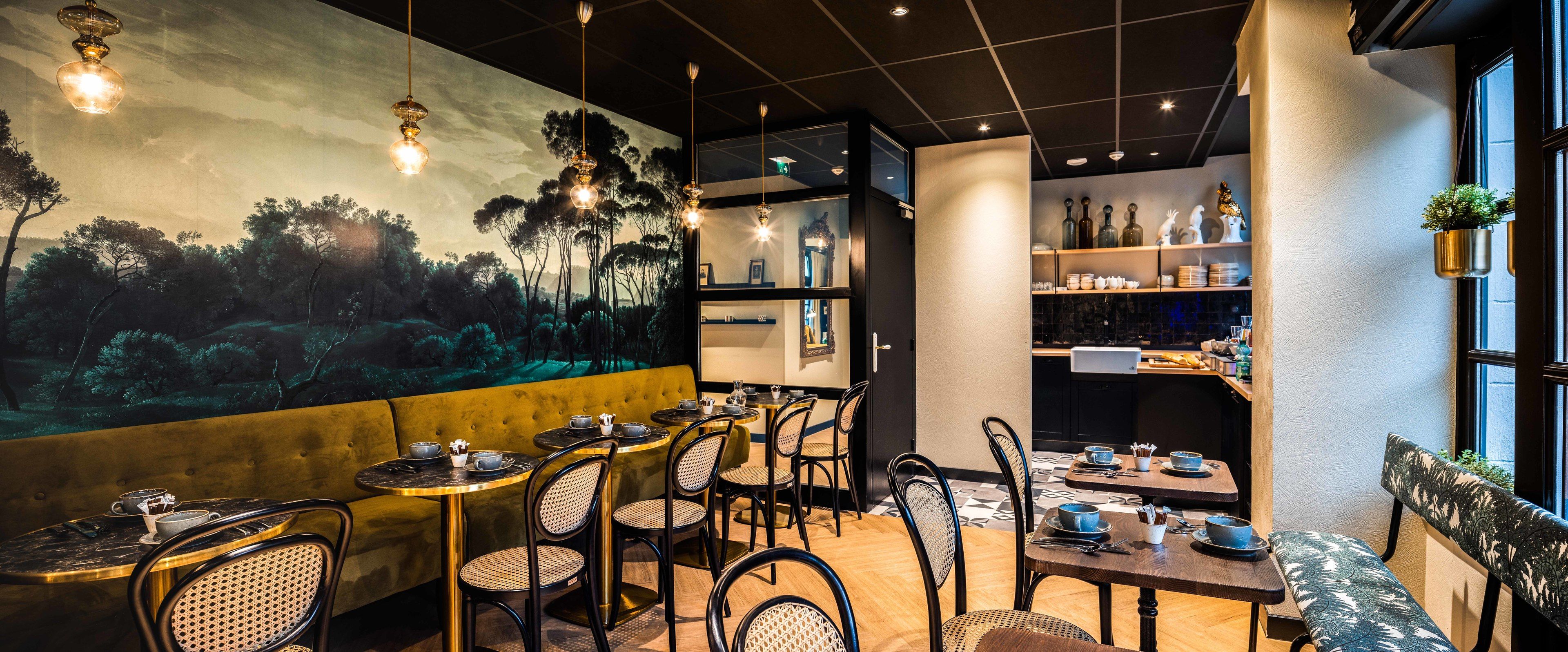 A restaurant with round tables, wicker chairs, a mural, and shelves with bottles and glasses.