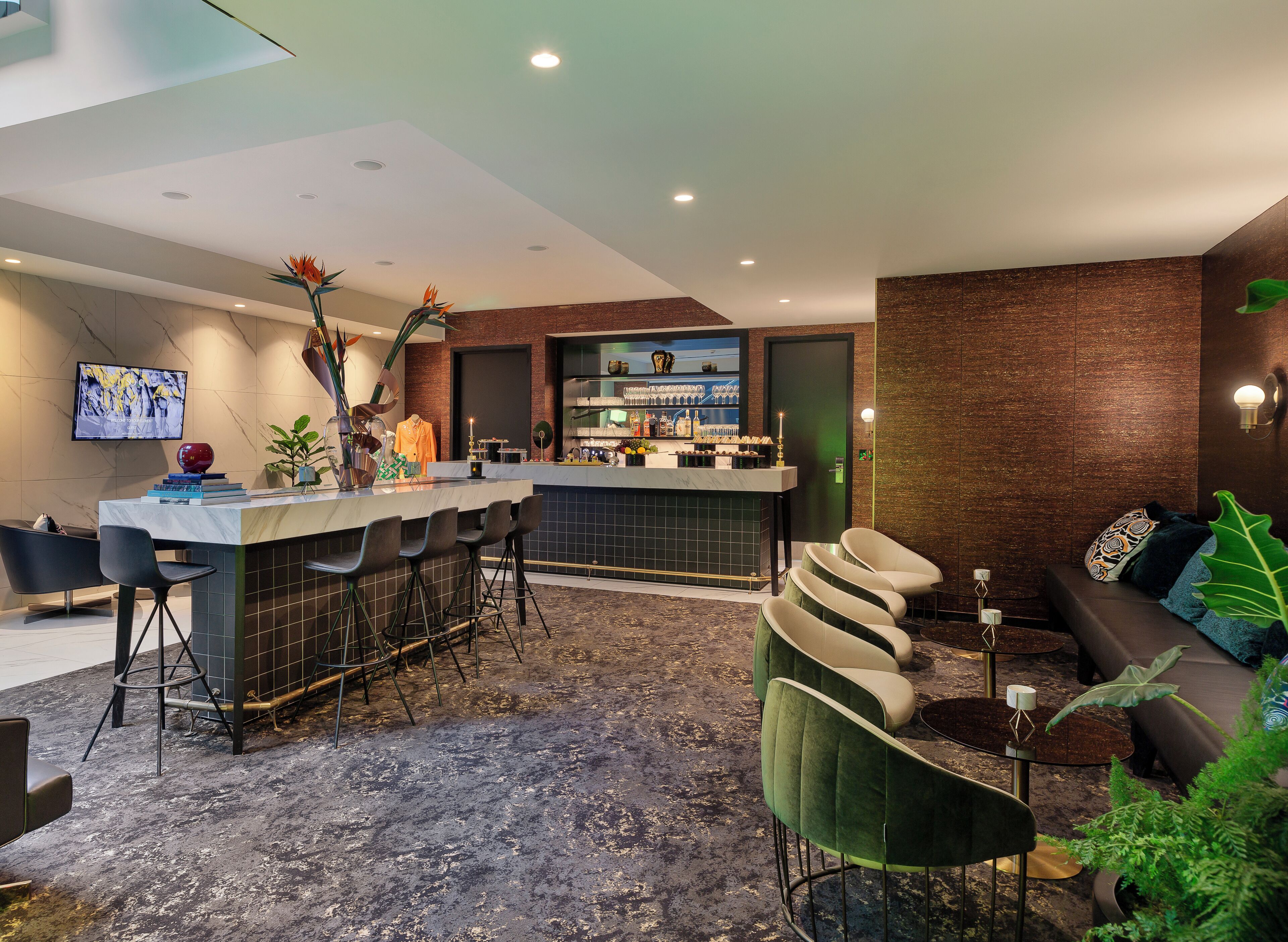 A modern bar area with a marble countertop, bar stools, and a television screen.