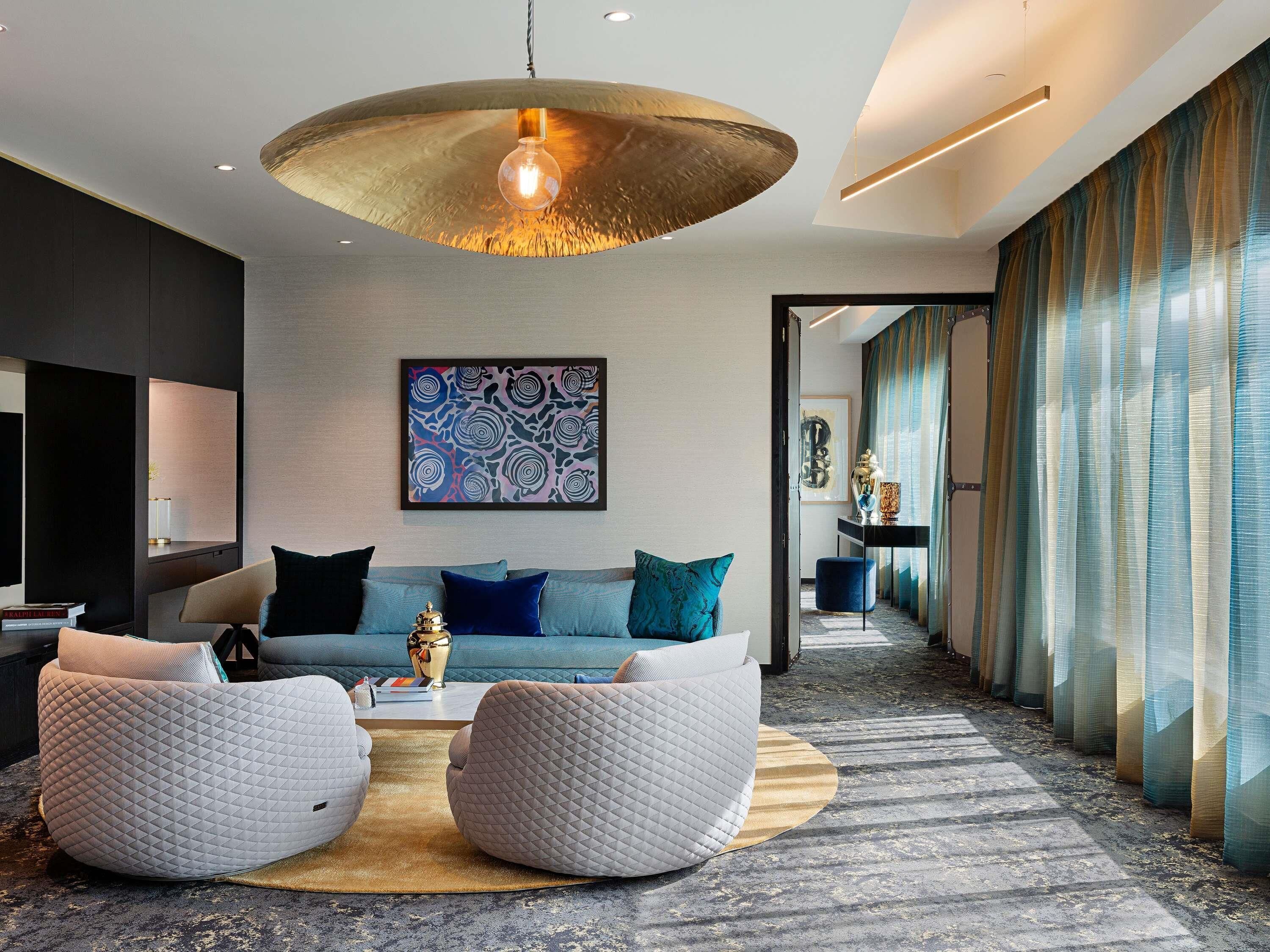 Una sala moderna con un sofá, dos sillones tipo pouf blancos, una mesita de centro y un cuadro abstracto grande en la pared.