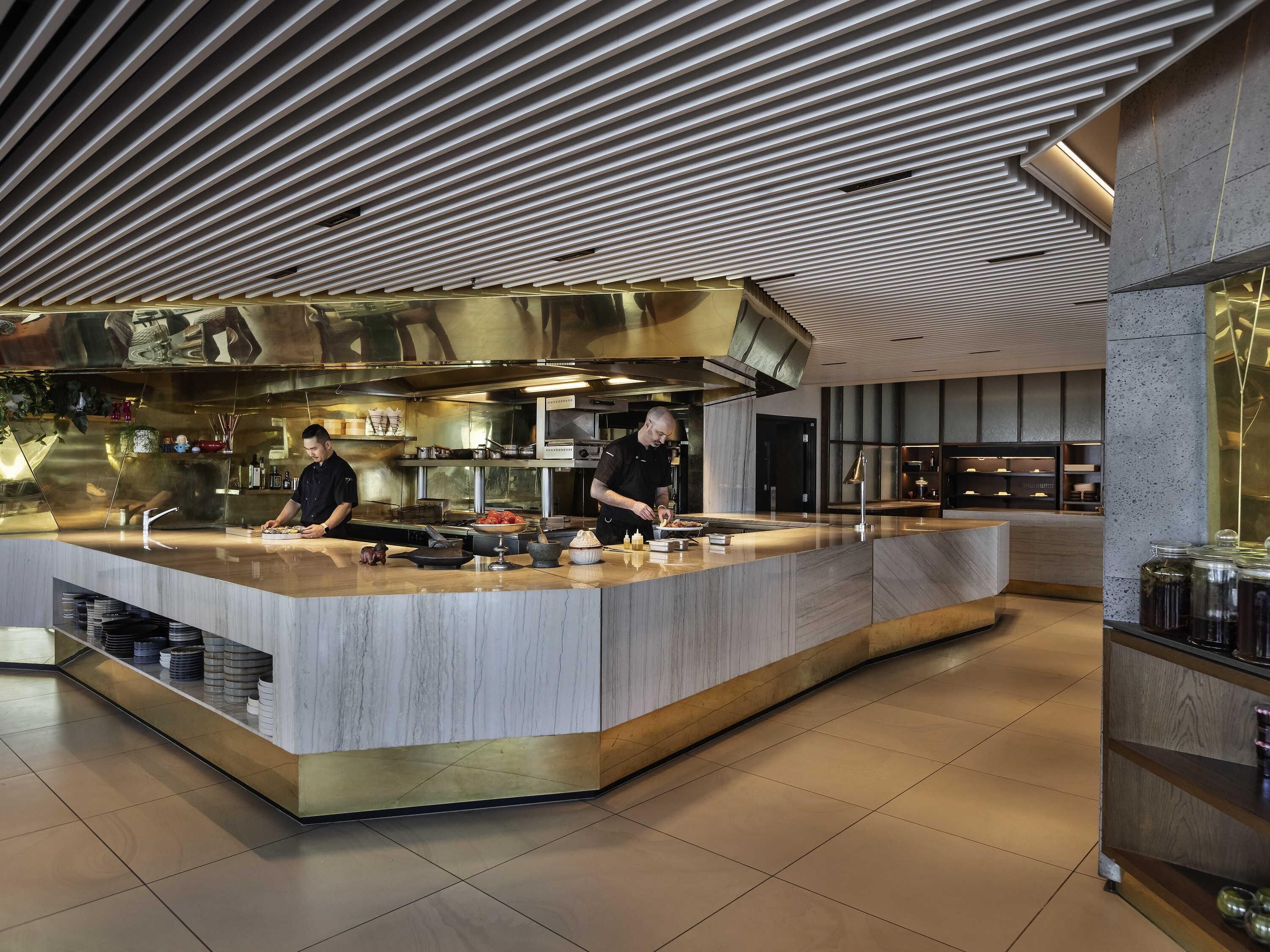 A modern kitchen with two chefs working at a central island, equipped with various cooking tools and appliances.