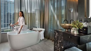A modern bathroom with a freestanding bathtub, a vanity with a marble countertop, and a large window with curtains. - SO/ Auckland (Auckland)