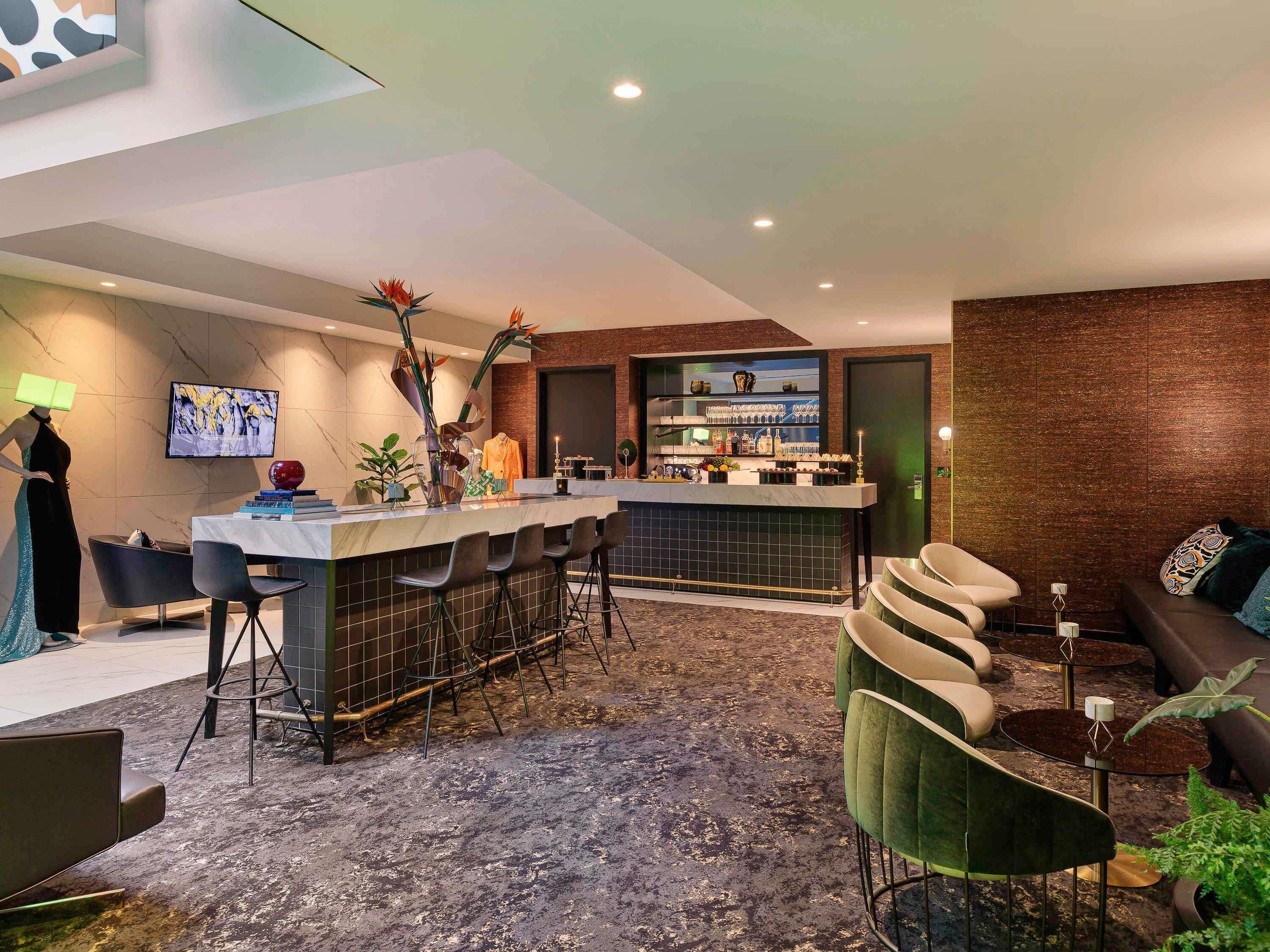 A modern bar area with a marble countertop, bar stools, and a television screen.