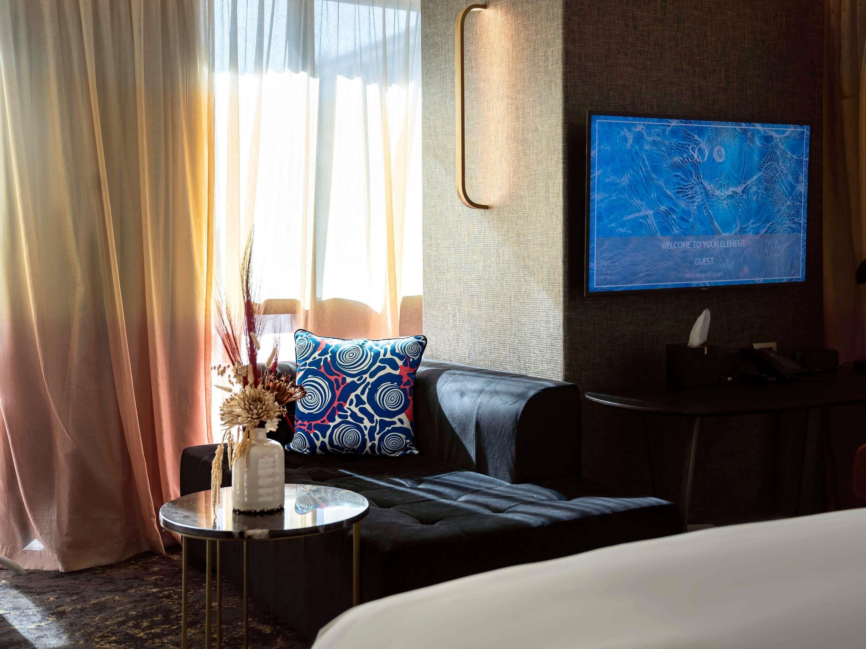 Une chambre d’hôtel avec un lit, un canapé, une petite table sur laquelle est posé un vase, et un téléviseur fixé au mur qui affiche une carte.