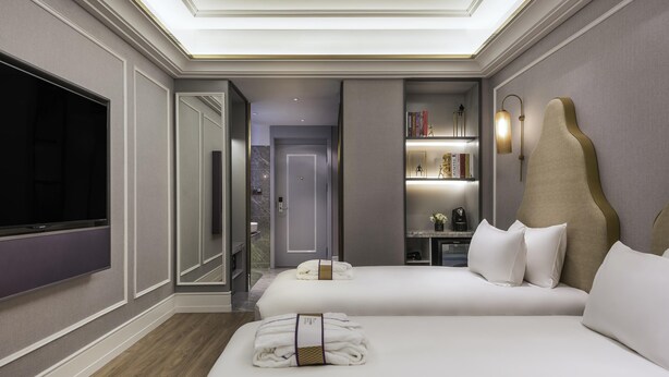 Ein Hotelzimmer mit zwei Betten, einem Fernseher, einem Bücherregal und einem durch eine geöffnete Tür einsehbaren Badezimmer.