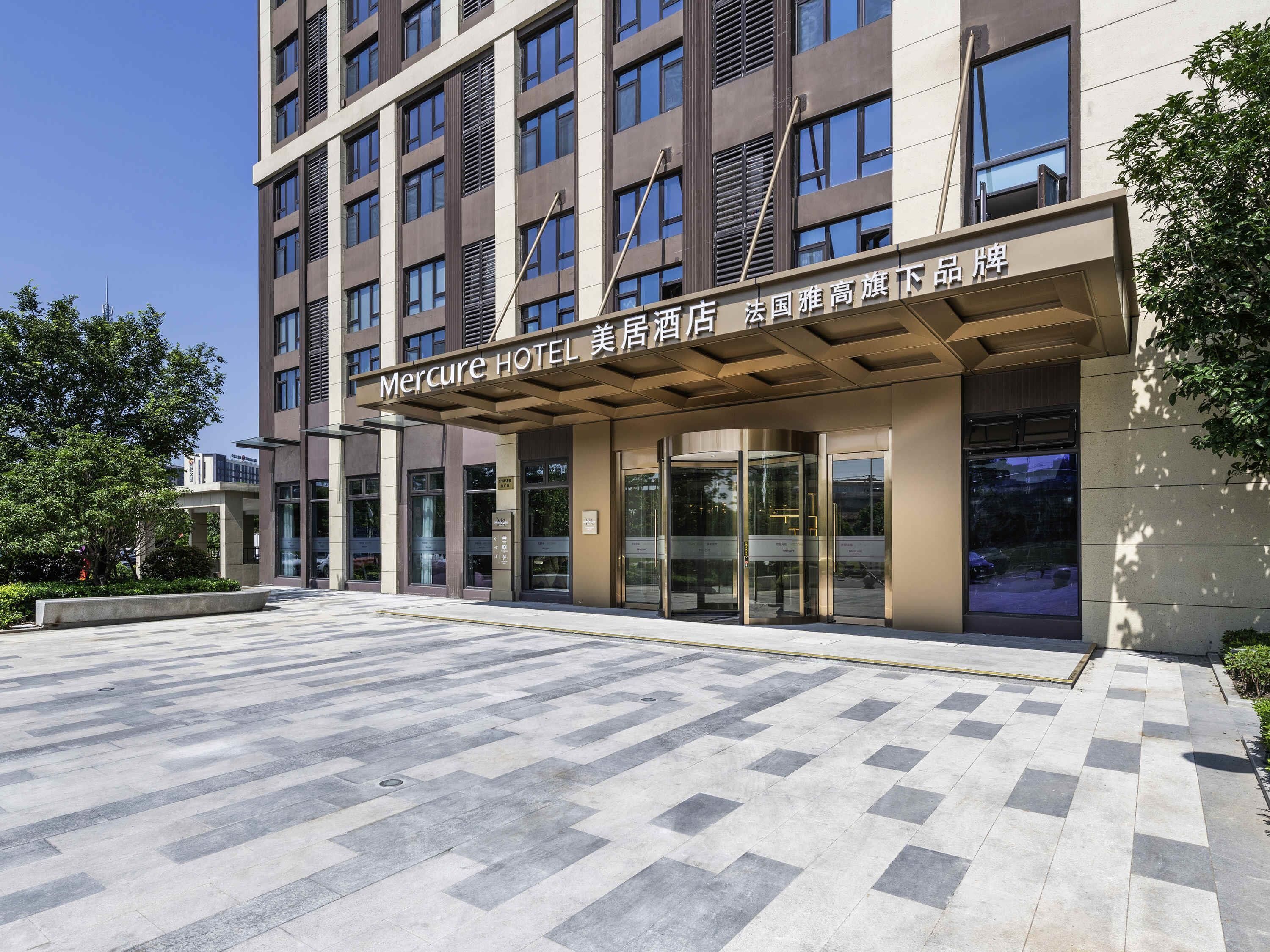 A hotel entrance with a modern design, featuring a large glass door, a covered entrance area, and a tiled pavement.