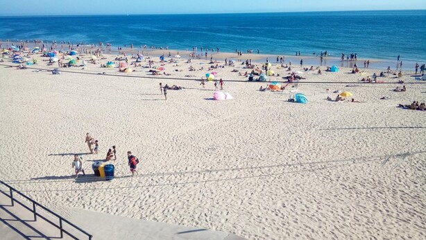 Une vaste plage où l’on peut voir des gens se prélasser au soleil et nager, sous un ciel bleu et dégagé.