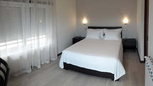Une chambre à coucher comprenant un lit, deux tables de chevet, une commode, une chaise et une fenêtre avec des rideaux.
