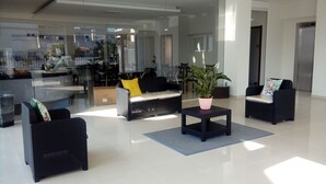 Un hall d’entrée moderne, avec des meubles en rotin noir, une plante en pot et une cloison en verre.