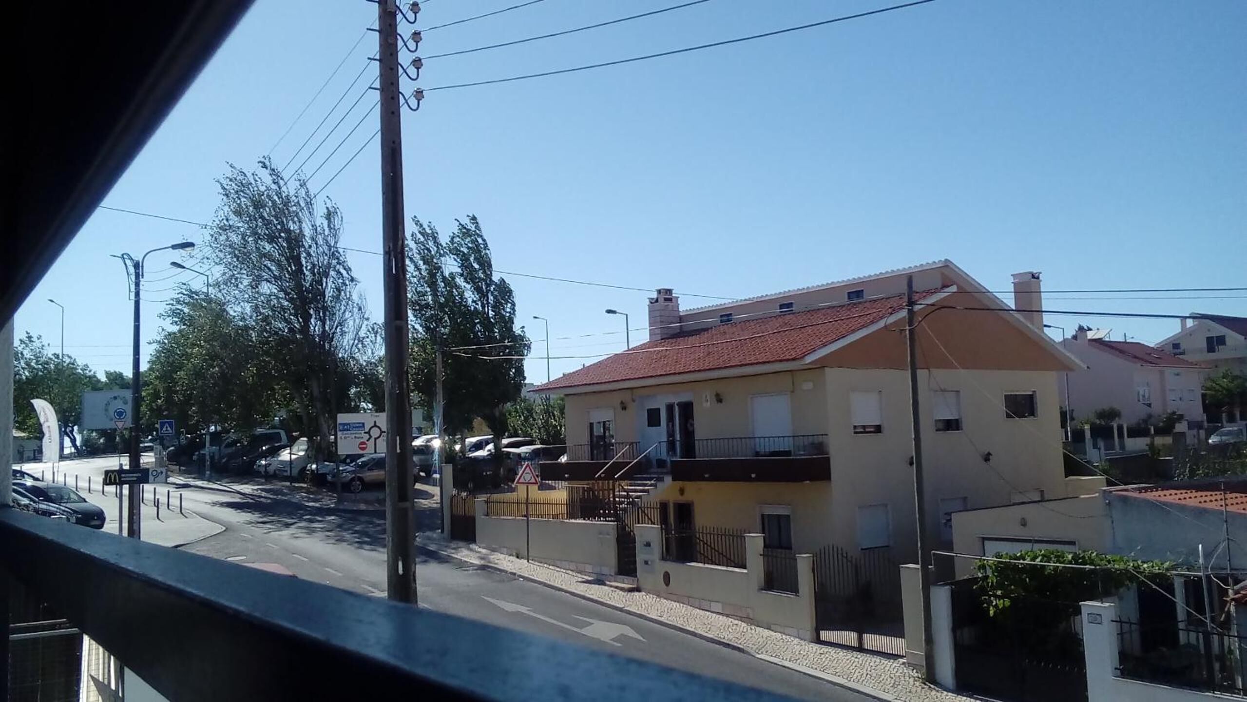 Uma rua residencial com casas, carros estacionados e céu claro.