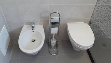 A bathroom with a bidet, a toilet, and a shower area.