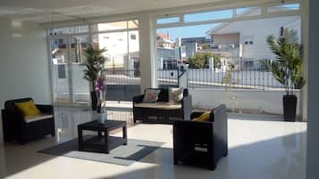A modern living room with a sofa, armchairs, and a coffee table. There are large windows offering a view of the street and buildings outside.