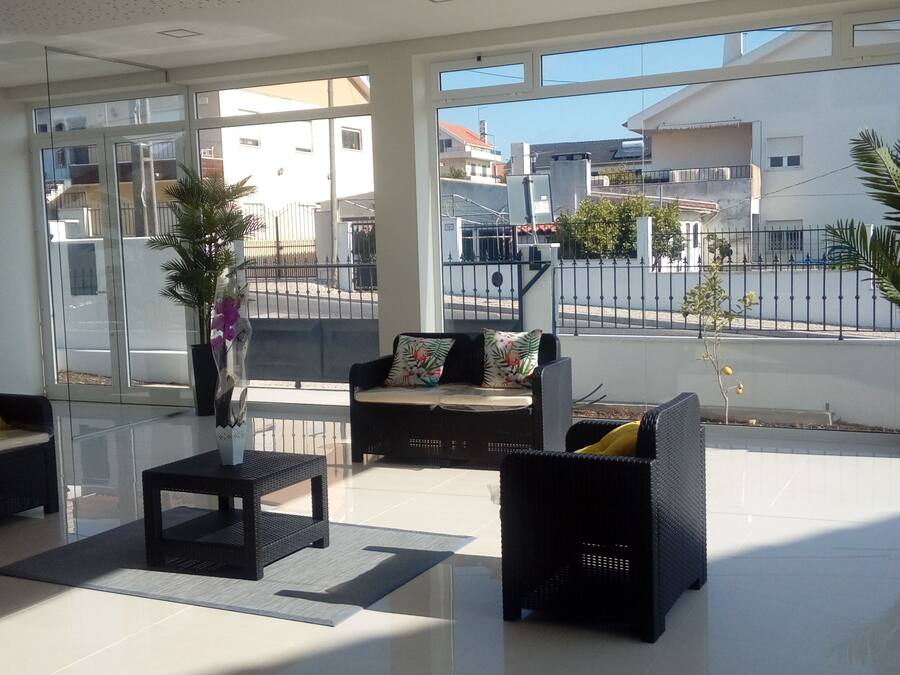 A modern living room with a sofa, armchairs, and a coffee table. There are large windows offering a view of the street and buildings outside.