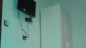 Une chambre avec un berceau blanc, un téléviseur fixé au mur et une armoire blanche.