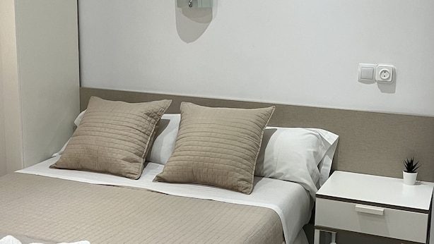 Une chambre bien rangée, avec un lit, une table de chevet et une prise électrique au mur.