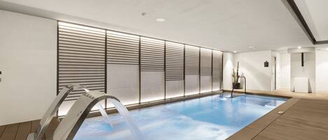 Ein moderner, überdachter Schwimmbereich mit Wasserspiel, Holzboden und minimalistischem Design.