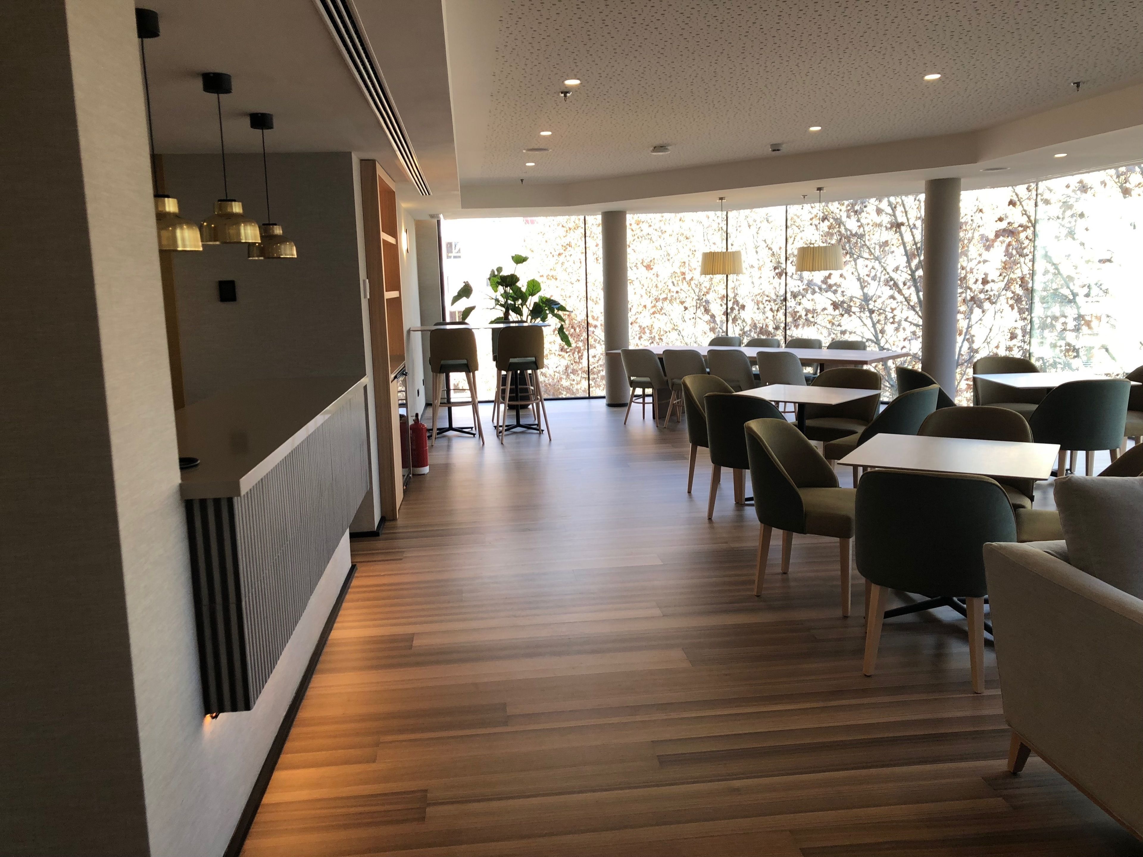 Un comedor moderno con suelo de madera, sillas contemporáneas e iluminación colgante.