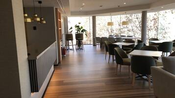 Un comedor moderno con suelo de madera, sillas contemporáneas e iluminación colgante.