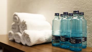 Un estante de madera con toallas blancas dobladas con esmero y varias botellas de agua Font Vella.