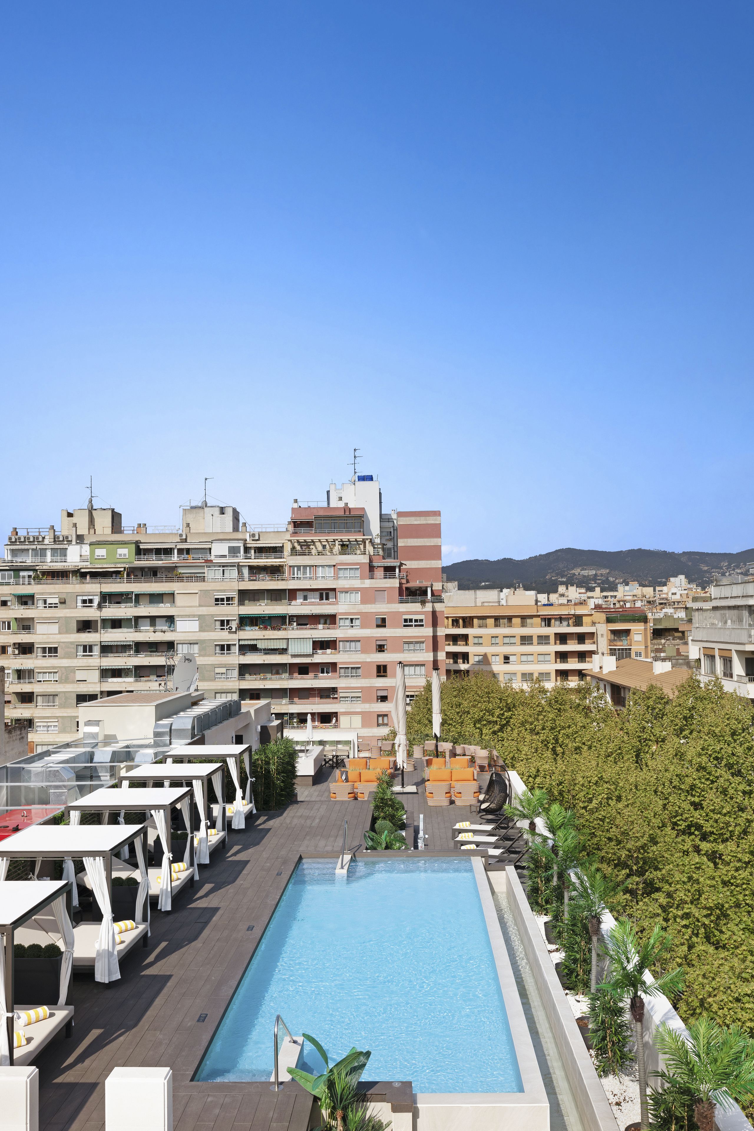 Une piscine sur le toit, dotée de chaises longues et offrant une vue sur un paysage urbain avec des bâtiments et des montagnes en arrière-plan.