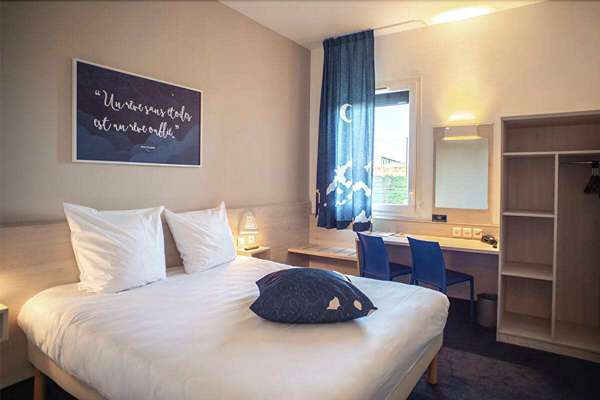 A hotel room with a bed, a desk, a chair, a wardrobe, and a window with a view.