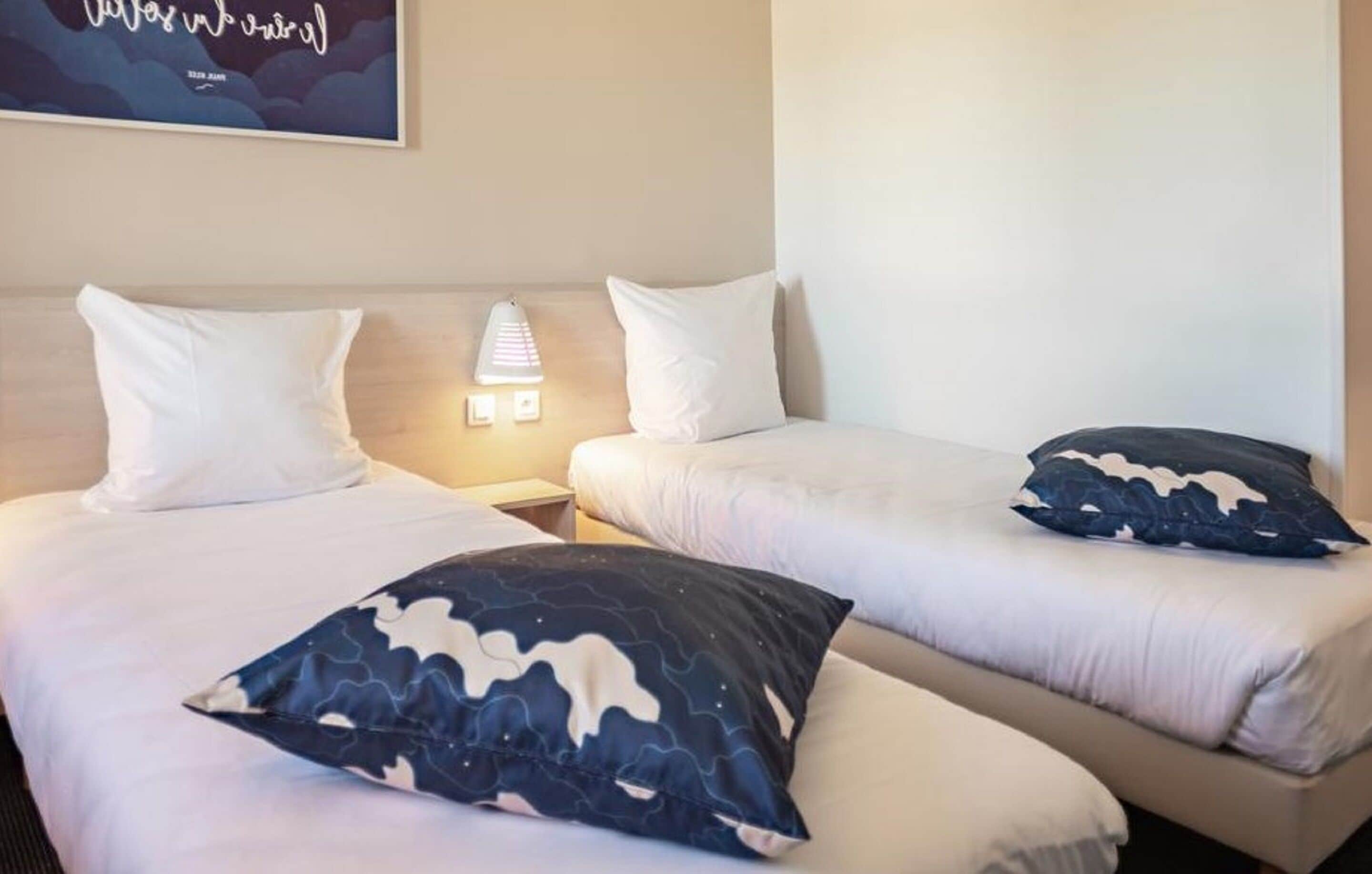 Two single beds with white bedding and a night lamp on the nightstand.