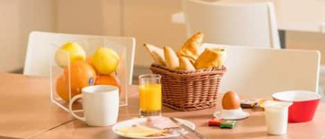 Una mesa de desayuno con una cesta de pan, una taza, un plato de huevos y un vaso de zumo de naranja.