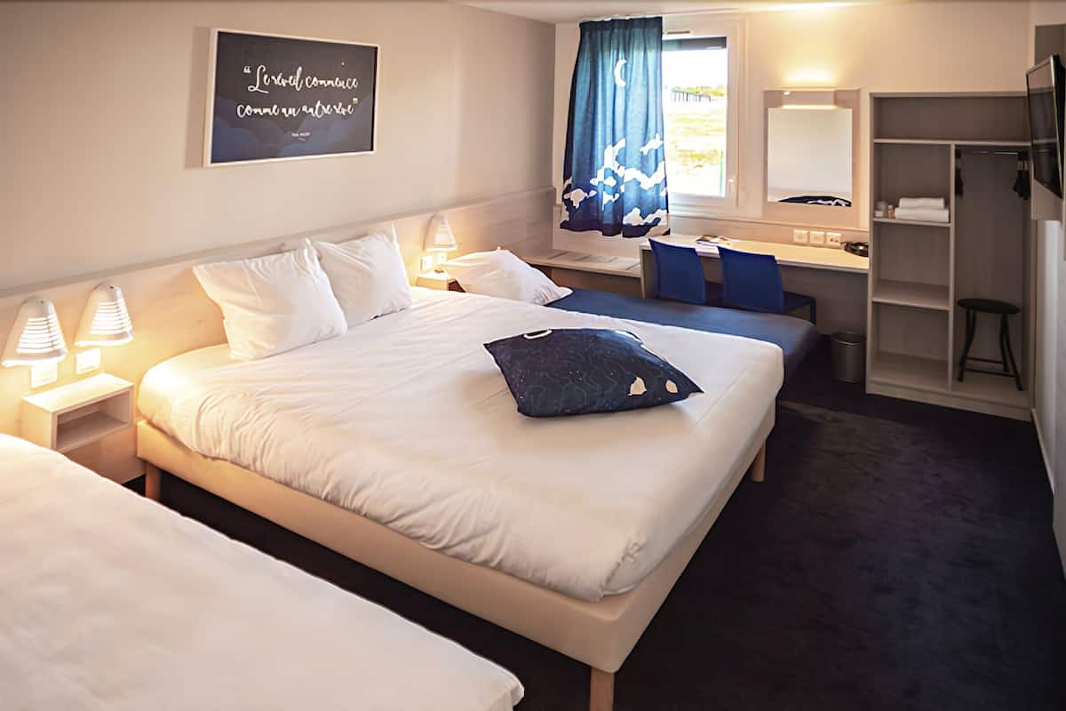 A hotel room with two beds, a desk, a chair, a mirror, and a wardrobe.