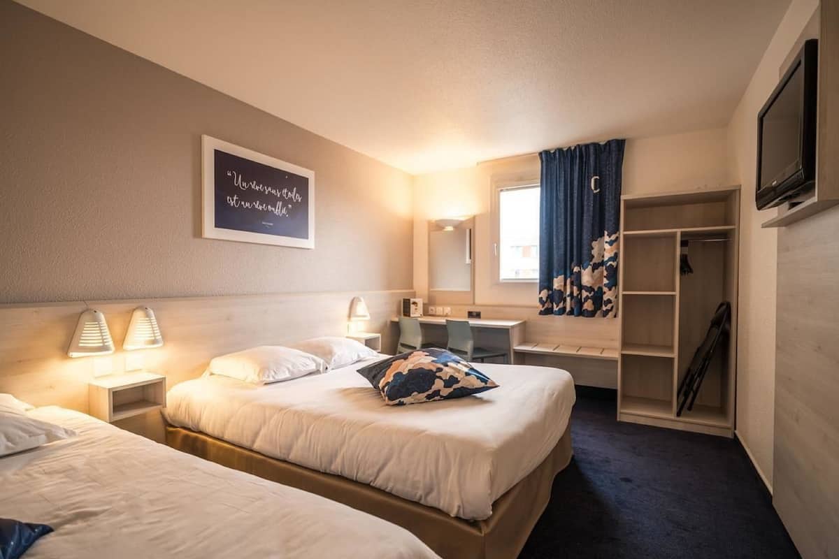 A hotel room with two beds, a desk, a mirror, a wardrobe, and a TV.