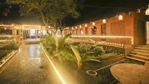 A well-lit outdoor area with a paved walkway, surrounded by lush greenery and wooden structures with circular windows. - Trang An Bungalow (Tay Hoa Lu)