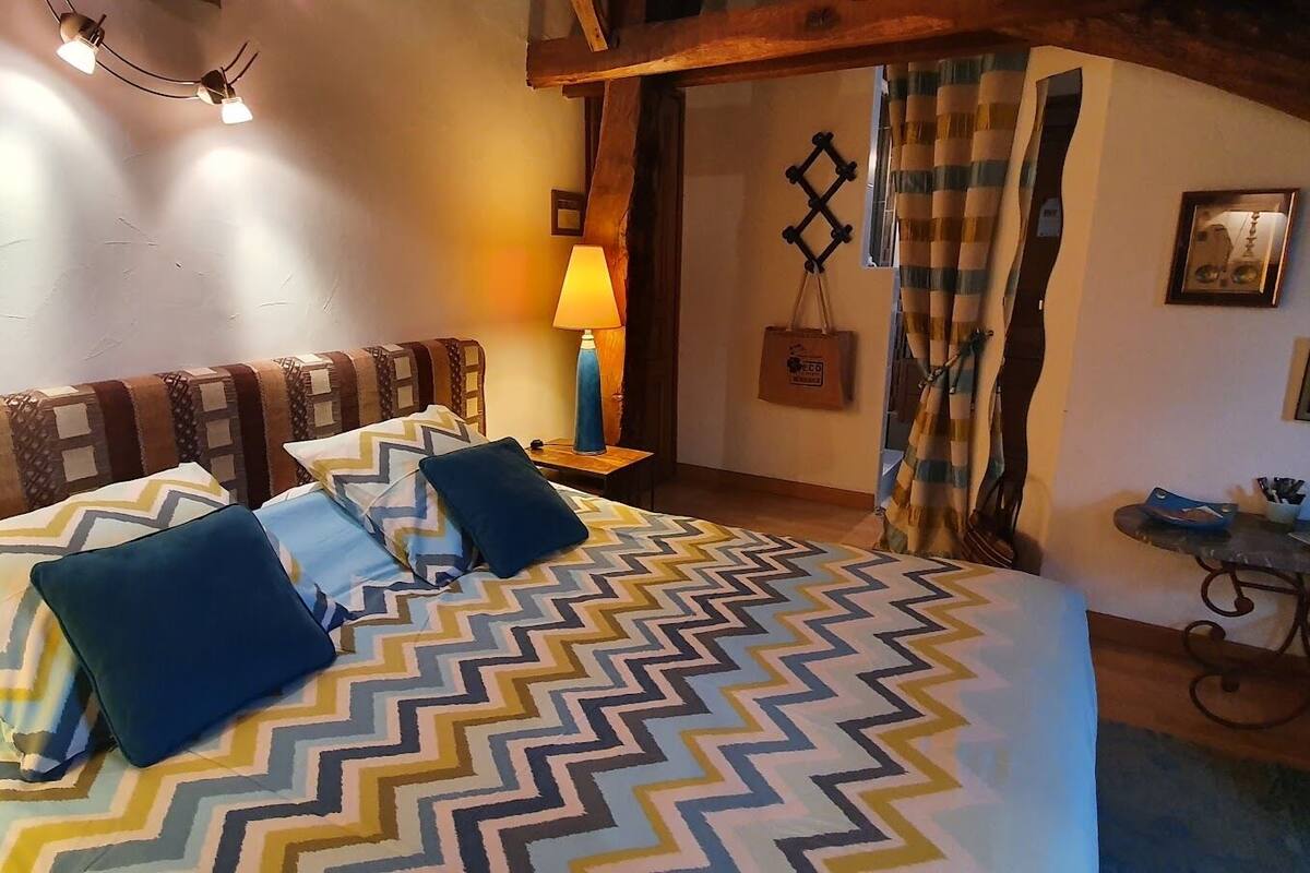 Un dormitorio acogedor con una cama grande, cabecera de madera, una lámpara de noche y una mesita con tazas y un cuenco.