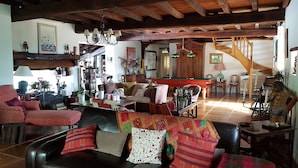 Amplia sala de estar con techo alto, vigas de madera, mesa de billar y un rincón de estar acogedor con sofá y sillones.