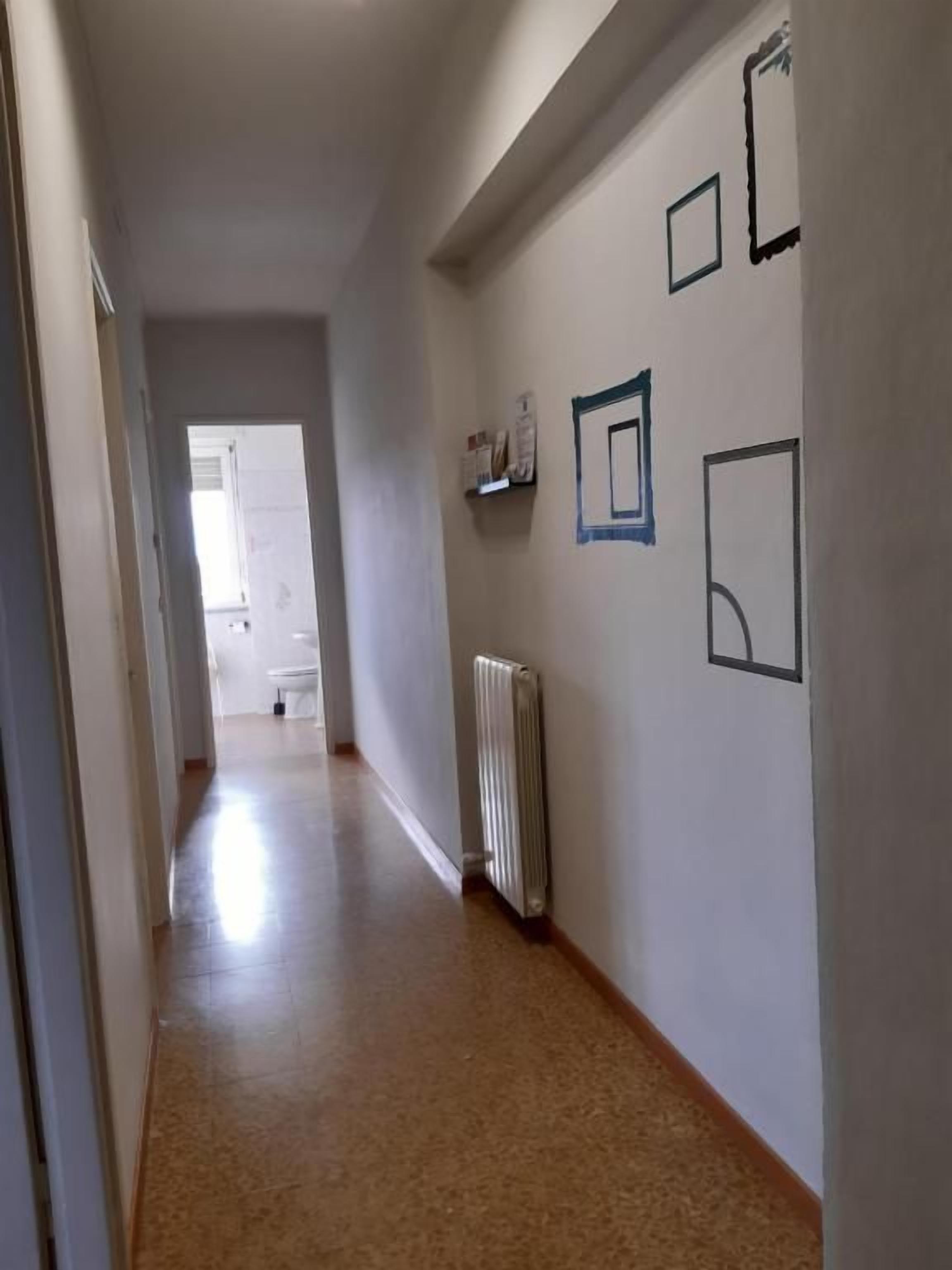 Un couloir avec un radiateur, une porte au fond et un mur orné de tableaux encadrés.