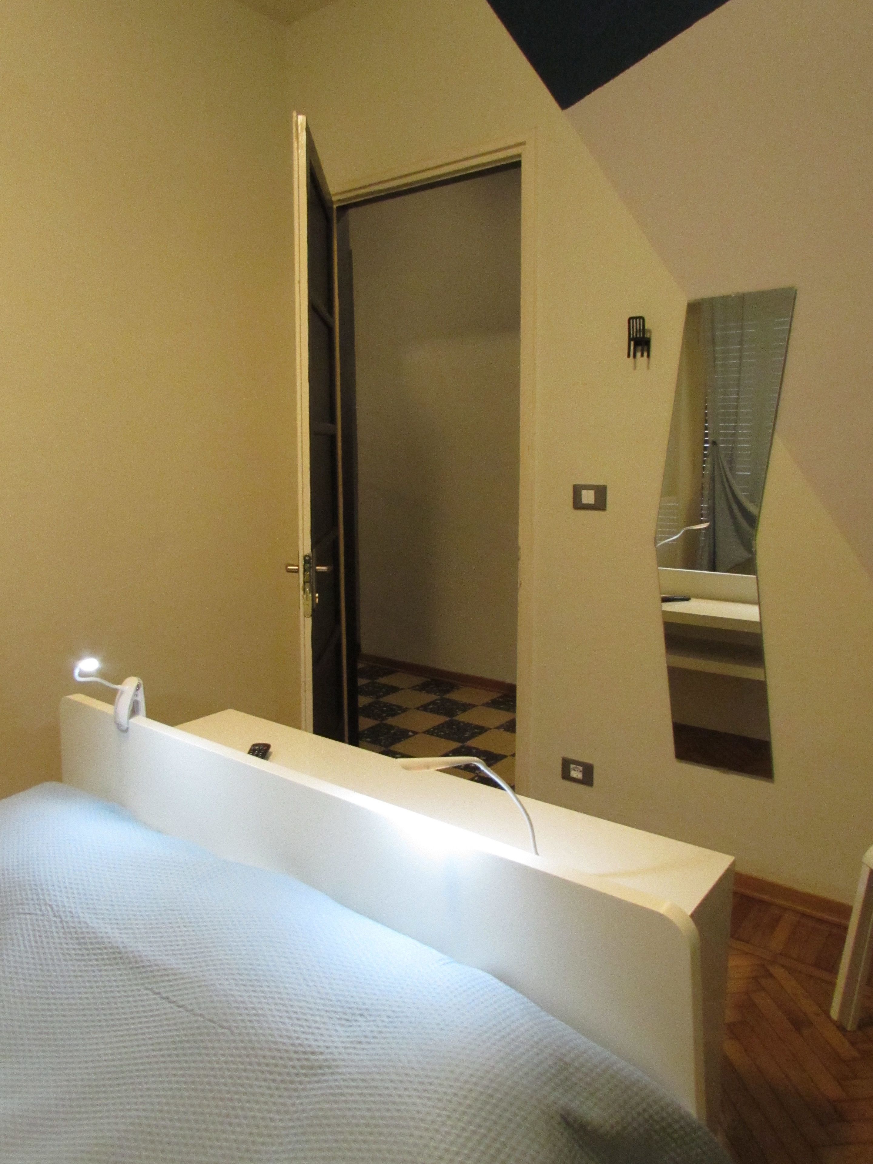 Un dormitorio con cama, mesita de noche, espejo y puerta que da a un baño.