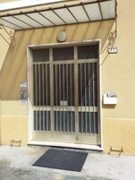 Fachada de edificio con una reja metálica, un buzón pequeño y un cartel con un número.