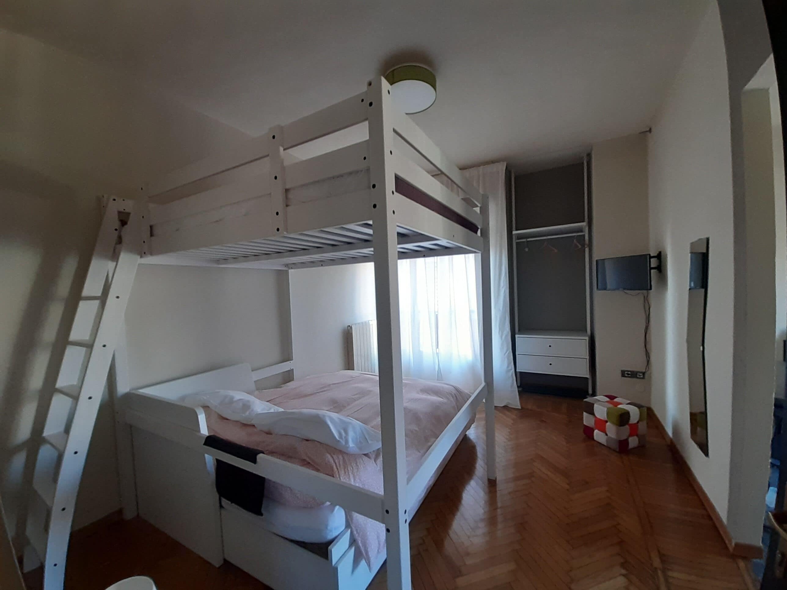 Ein Schlafraum mit Etagenbetten, einer kleinen Sitzecke und einem Fernseher an der Wand.