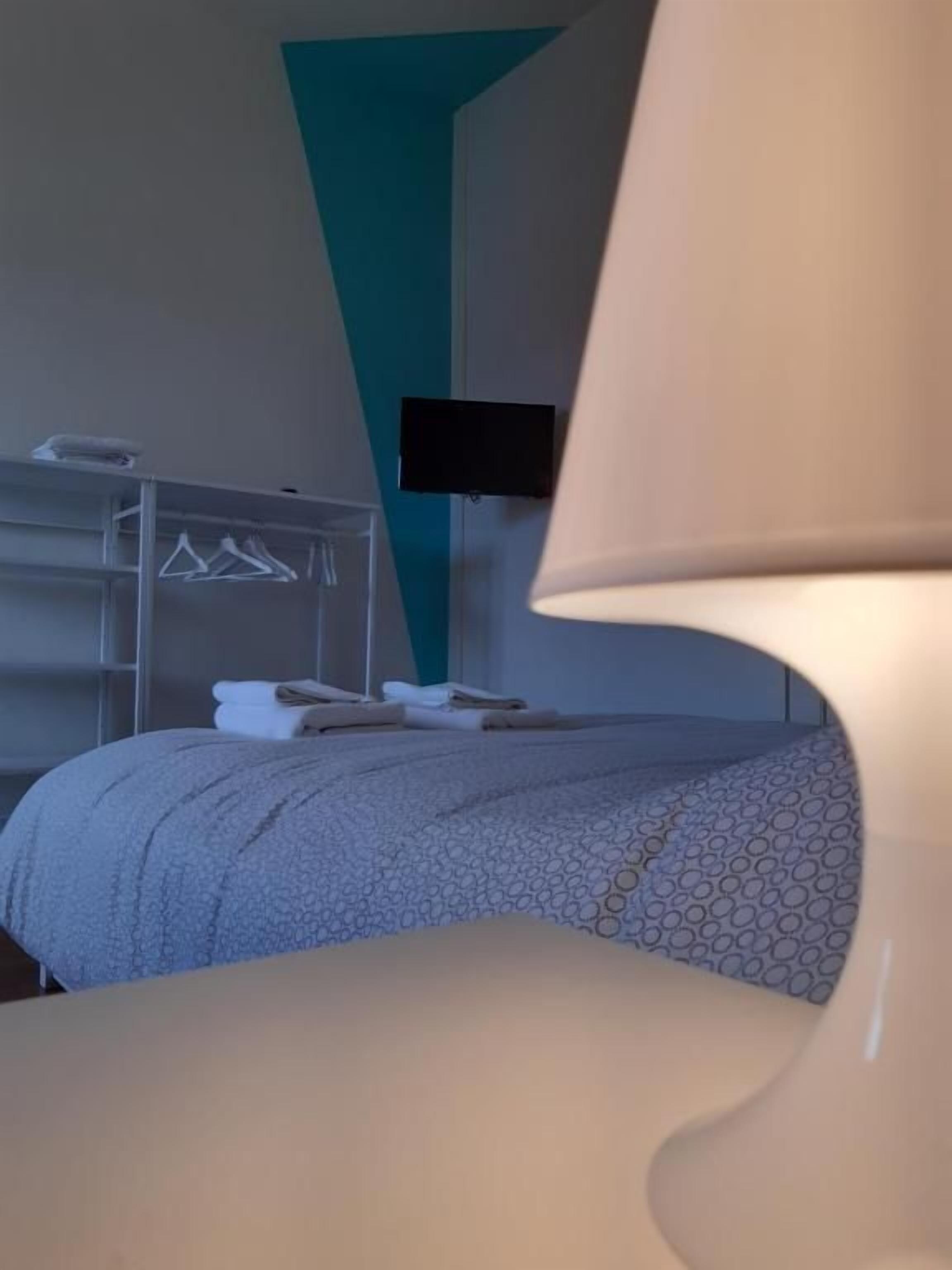 Une chambre d’hôtel comprenant un lit, une table de chevet, une lampe, un téléviseur fixé au mur et une armoire avec des cintres.