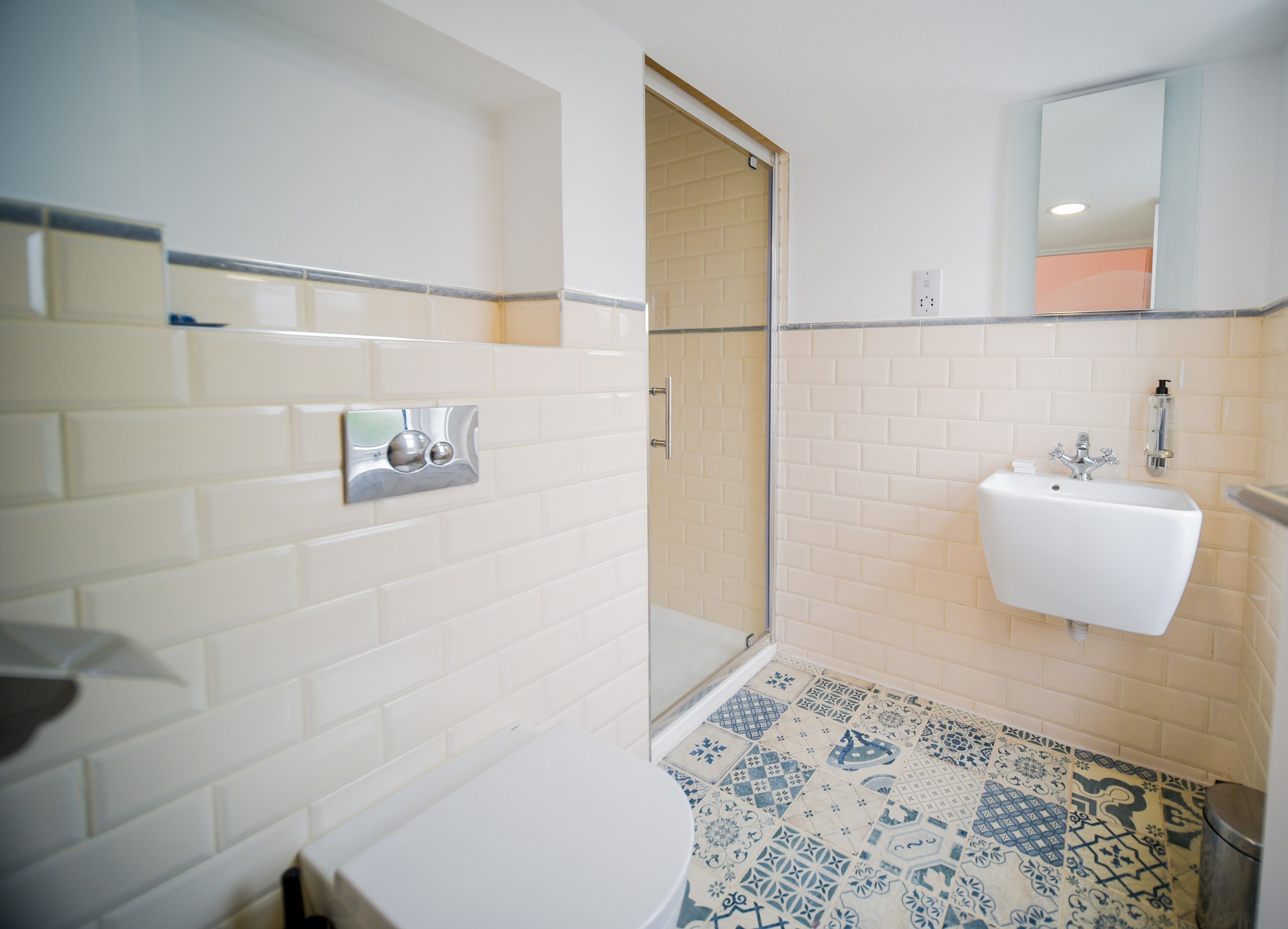 A bathroom with white subway tiles, a white sink with a mirror above it, and a shower area.