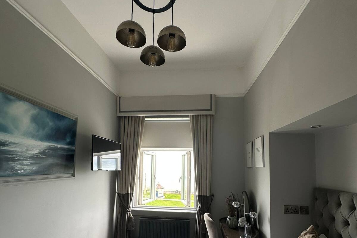Habitación de hotel con cama, escritorio, silla, ventana con cortinas y un cuadro en la pared.