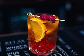 Un verre orné d’un motif rouge, contenant une boisson et décoré d’une tranche de citron et d’une framboise.