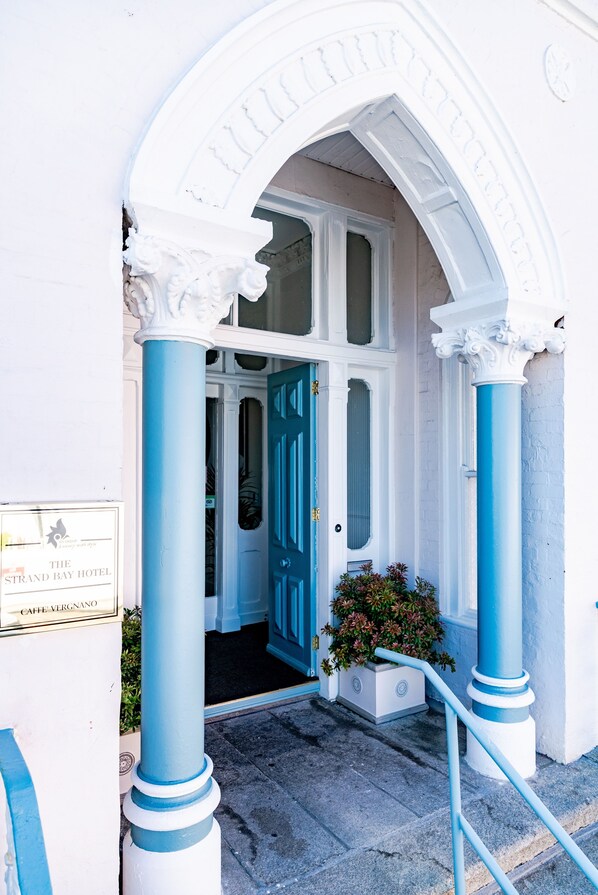 A hotel entrance with a blue and white facade, a signboard, and a potted plant. - The Strand Hotel, the former residence of Oscar Wilde (Bray)