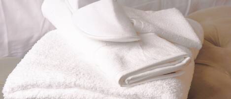 Una toalla blanca doblada con cuidado y un albornoz blanco sobre un sofá color beige, sobre un fondo blanco.