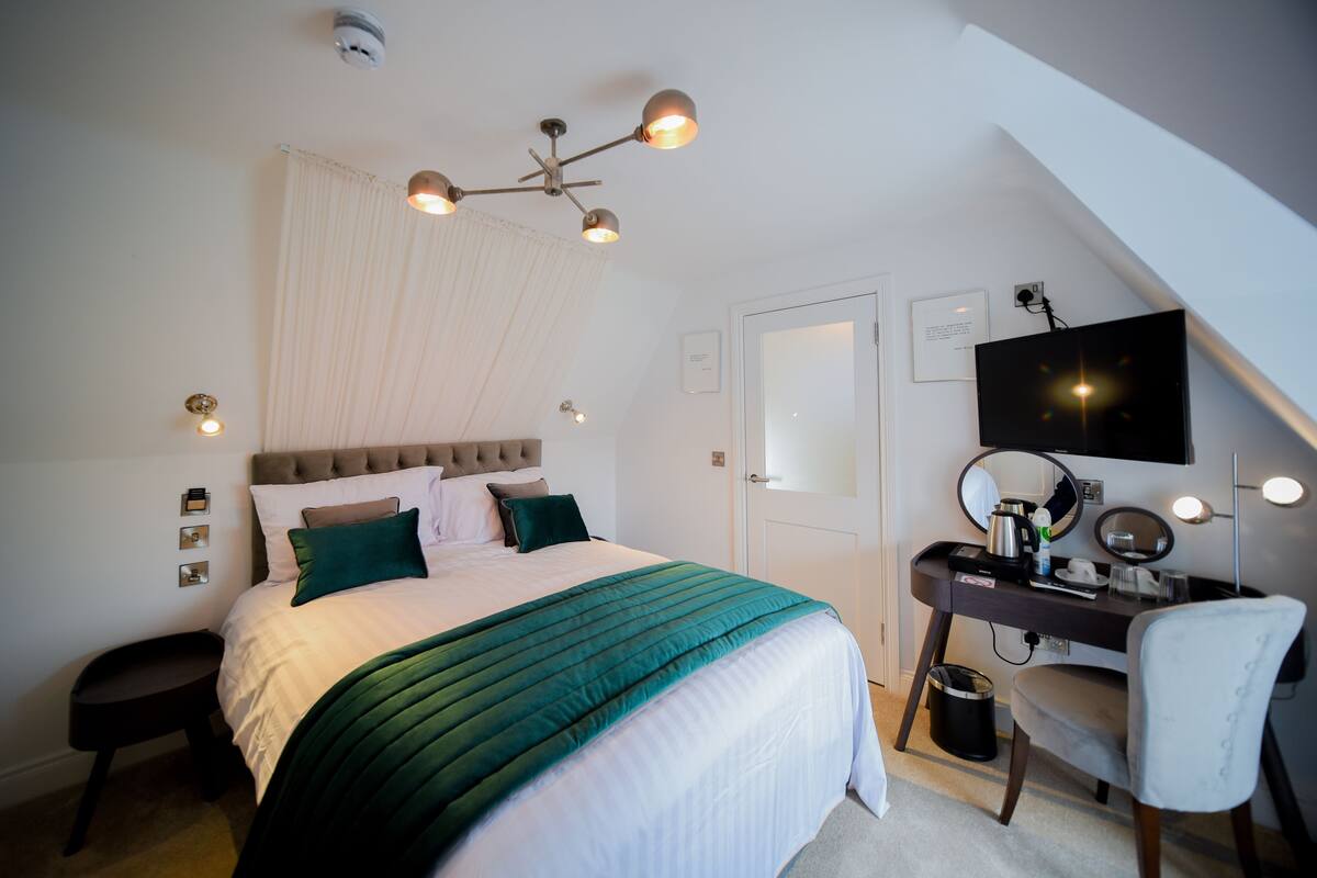 Un dormitorio con cama, escritorio, silla, televisor y ventilador de techo.