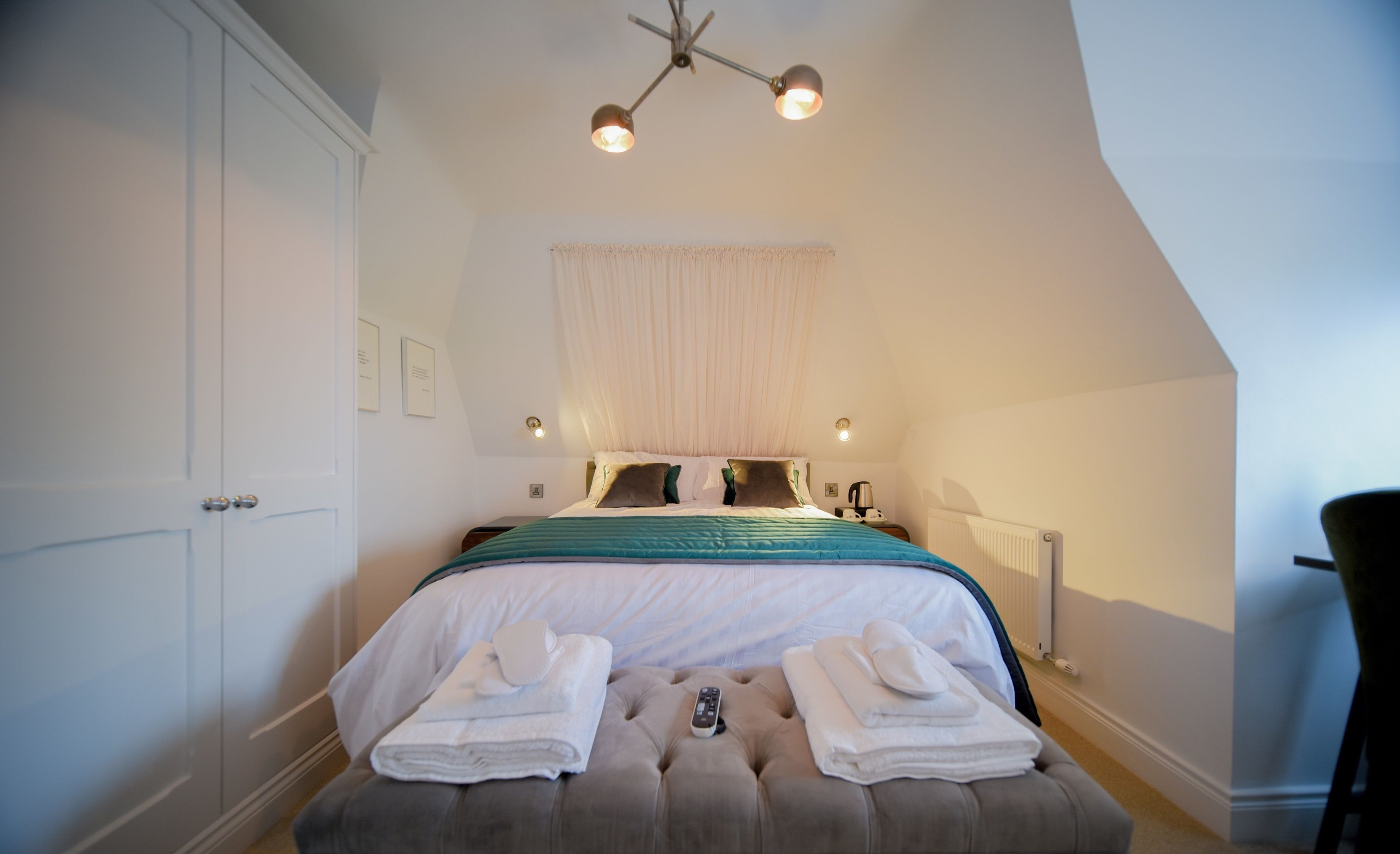 A bedroom with a bed, bedside lamps, a ceiling light, a window with curtains, and a chair.