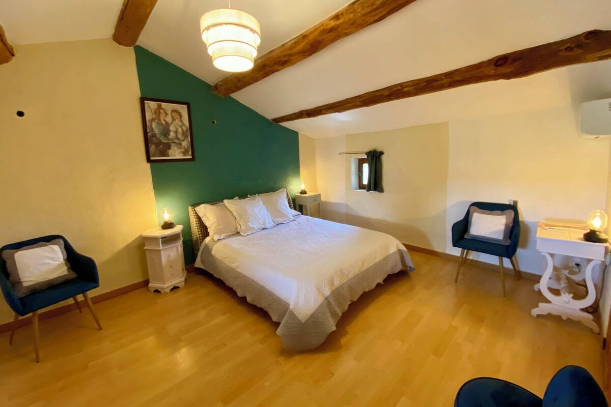 Ein Schlafzimmer mit einem Bett, Nachttischen, einem Sessel, einem Schreibtisch und einer Pendelleuchte.
