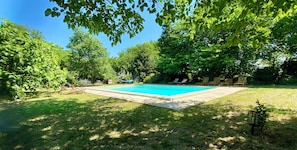 A rectangular swimming pool surrounded by grass and trees, with lounge chairs and a hammock. - B&B Le Mas de la Soie (Violes)