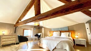 Une chambre avec un grand lit, des poutres en bois, un bureau et une chaise.