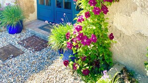 Un bâtiment doté d’une entrée en arc bleu, d’un mur en pierre et d’un pot de fleurs contenant des fleurs violettes.