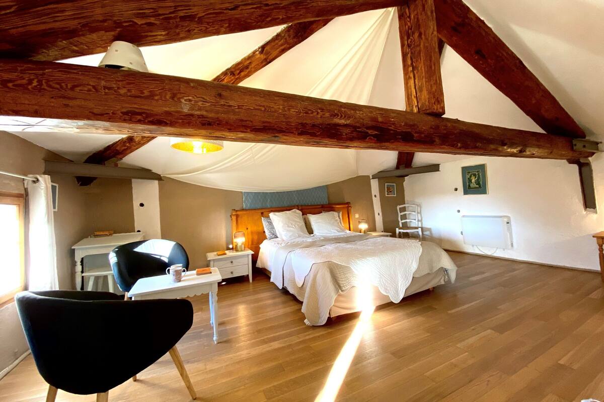 Ein gemütliches Schlafzimmer mit einem großen Bett, einem Schreibtisch und einem Stuhl. Die Decke ist aus Holz und es gibt einen weißen Baldachin.
