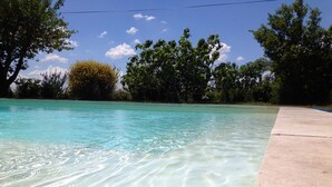 Une piscine aux eaux cristallines, bordée de béton, entourée d’arbres et surplombée d’un ciel dégagé.