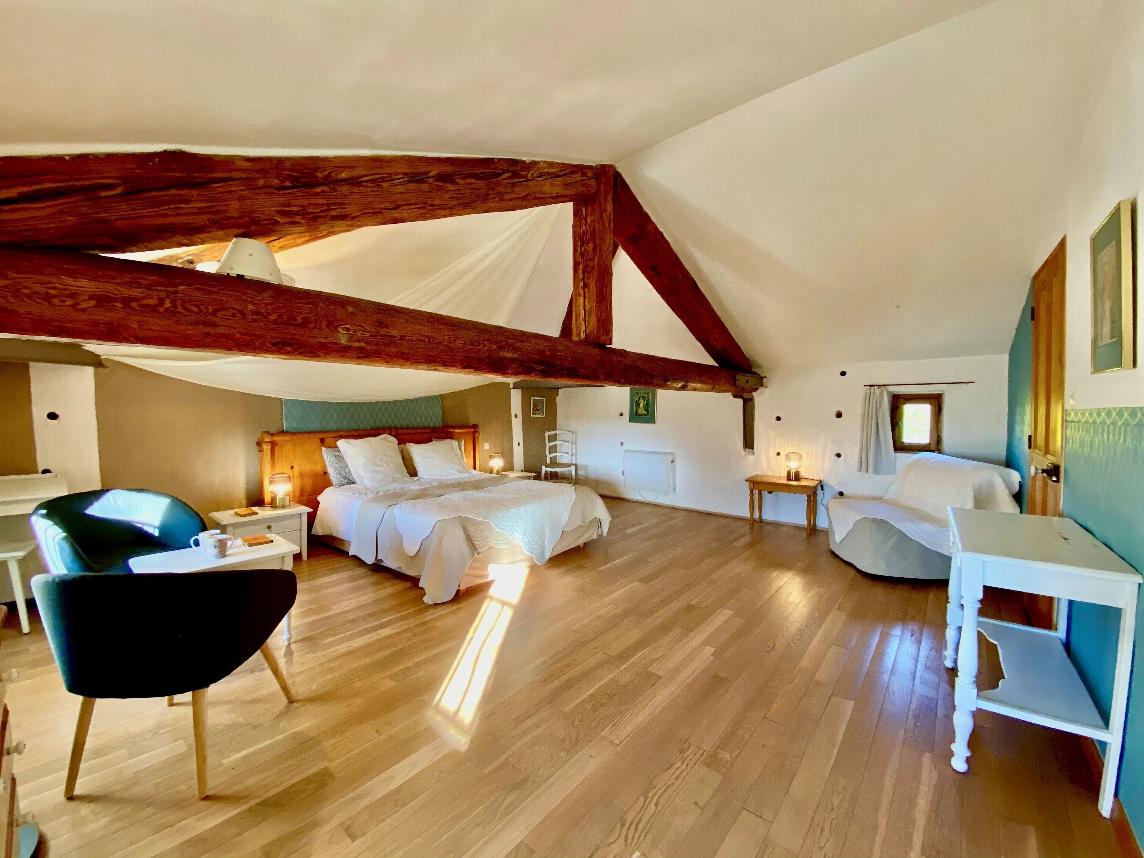 A spacious attic bedroom with a large bed, a chair, a small table, and a desk.